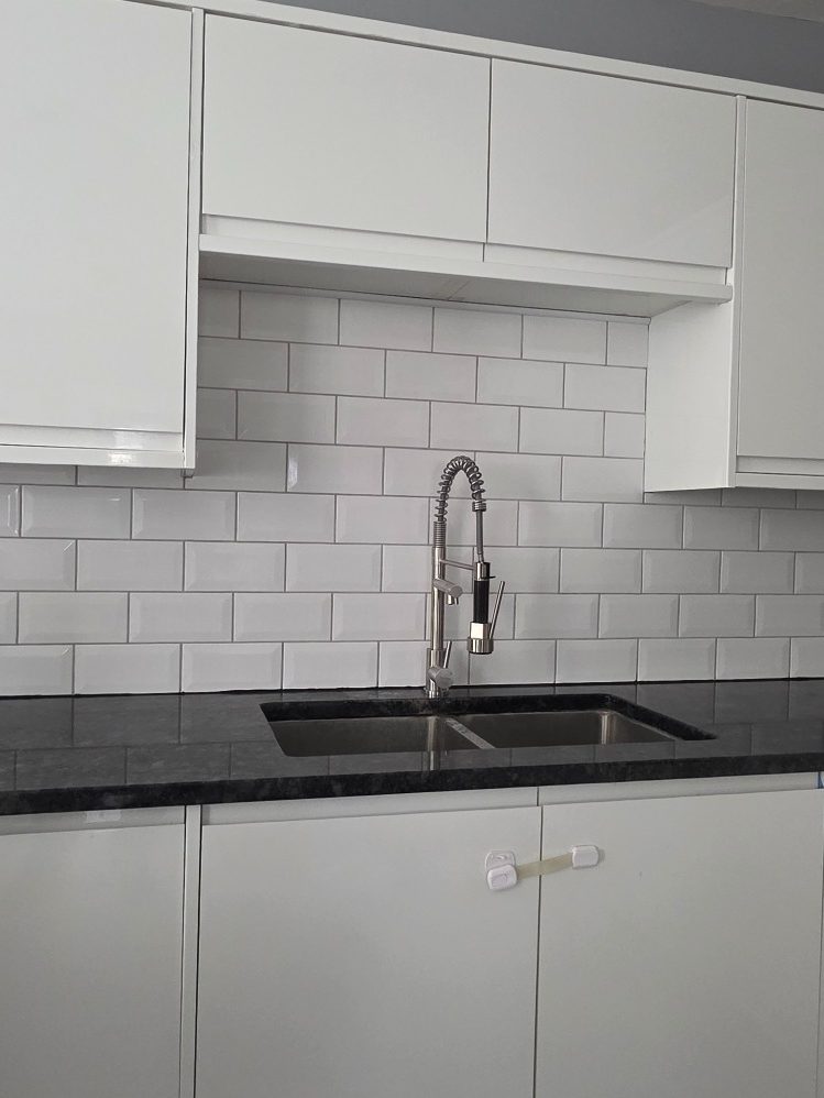 White subway tiled backsplash Subway style white ceramic tiles laid along a countertop behind a kitchen sink as a backsplash with light grey grout between.