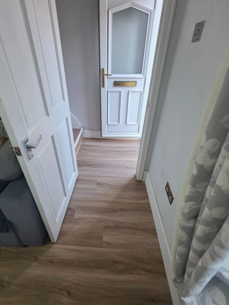 LVP flooring Oak effect LVP flooring laid seamlessly from a front door, at the bottom of stairs, all the way into a living room.